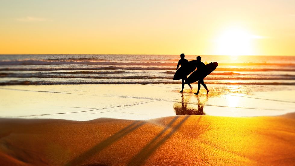 Two surfer running on the beach at sunset. Portugal